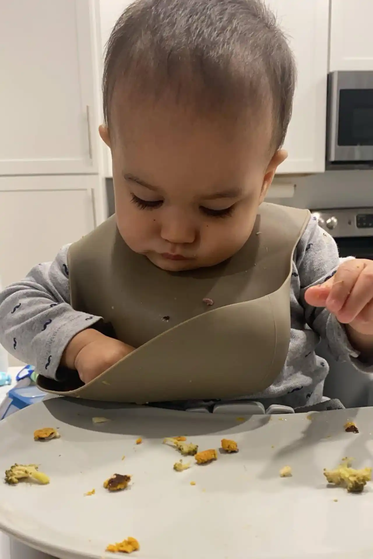 Baby boy eating finger food from bib